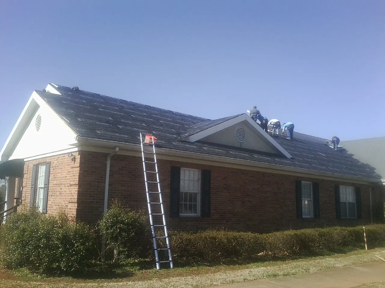Crew tearing shingles off a brick ranch roof with a ladder set — Emergency Roof Repair work by our crew in Bargersville