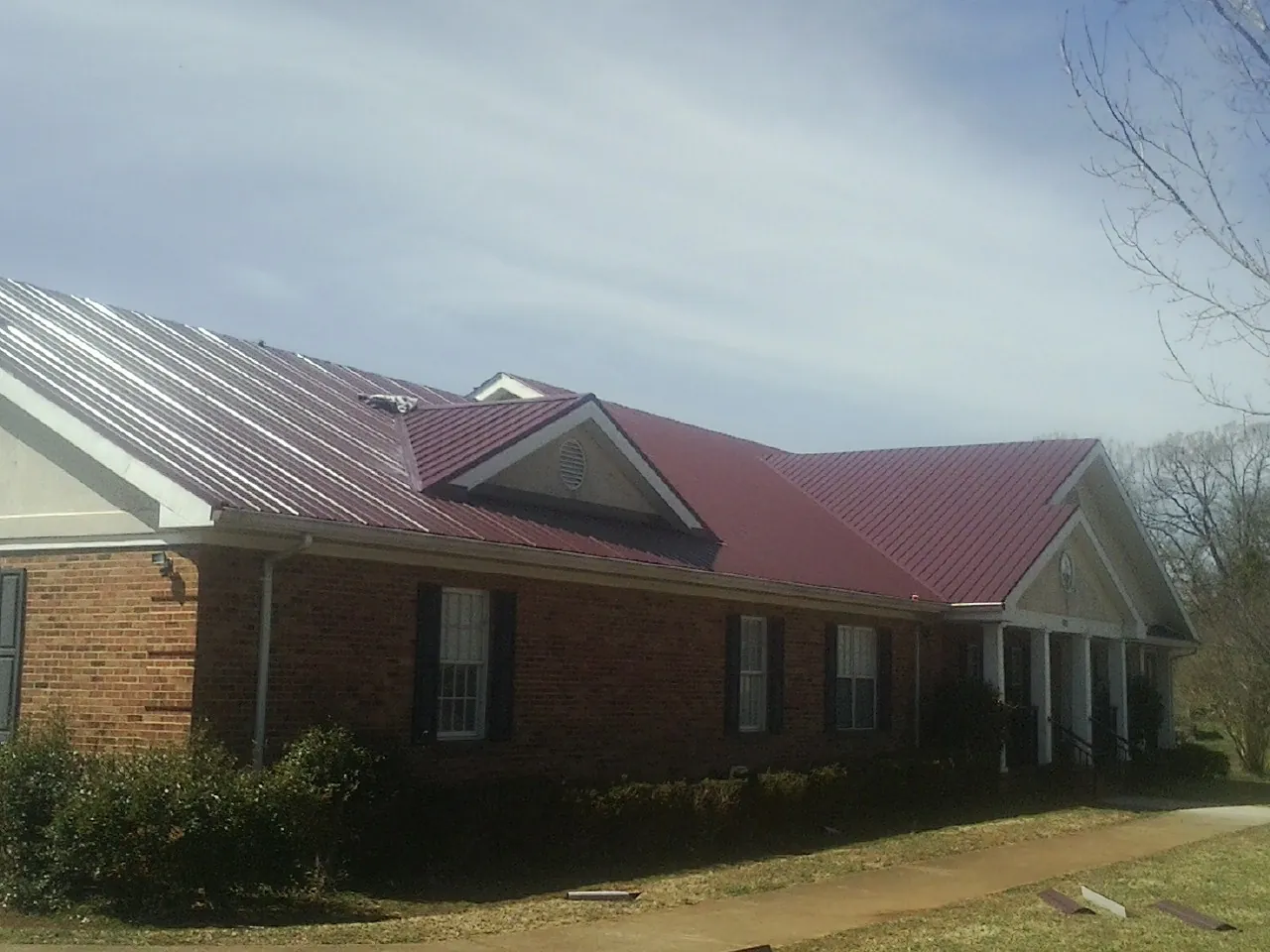 Red metal roof with gabled entries on a long brick building, from a Hail Damage Roof Repair job in Bargersville