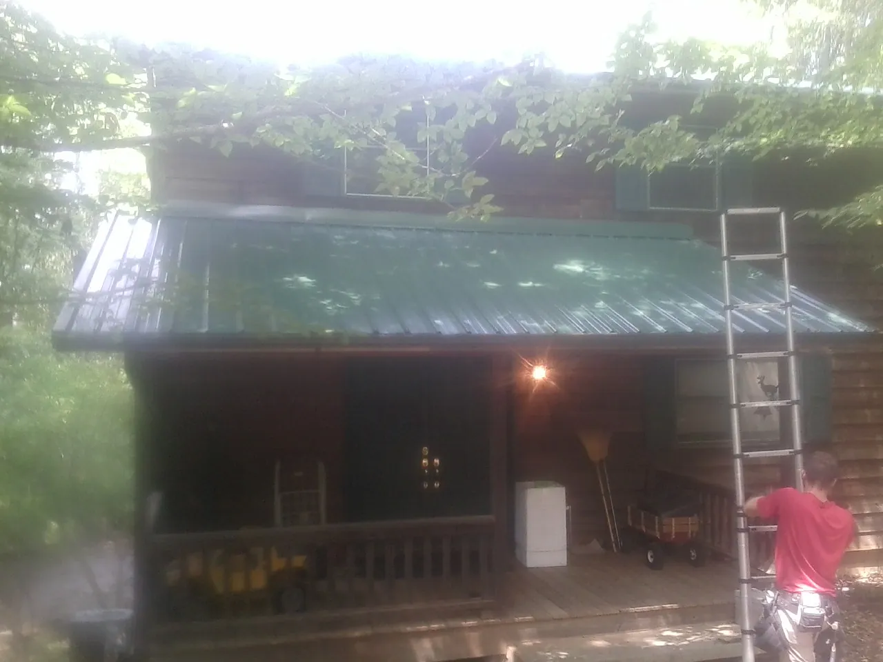 Worker on a ladder at the green porch roof of a wooded cabin in Bargersville