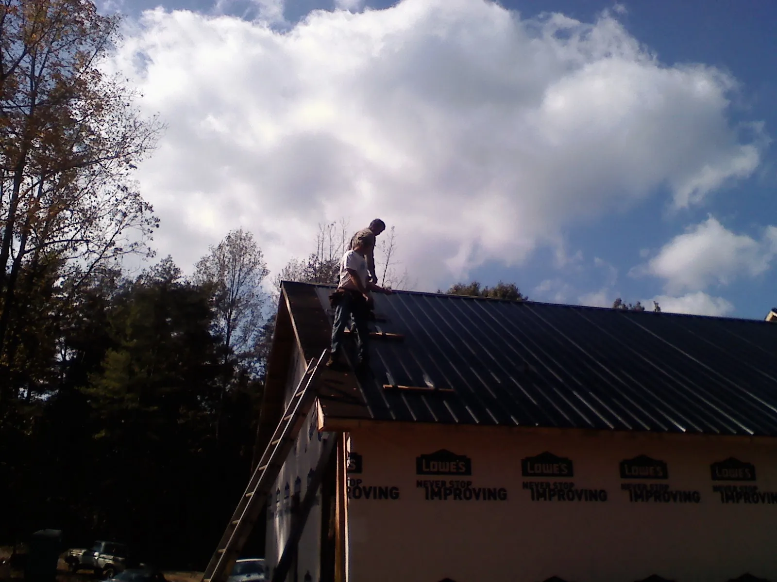 Roofer fastening dark metal panels high against a cloudy sky, from a Roof Inspection job in Bargersville