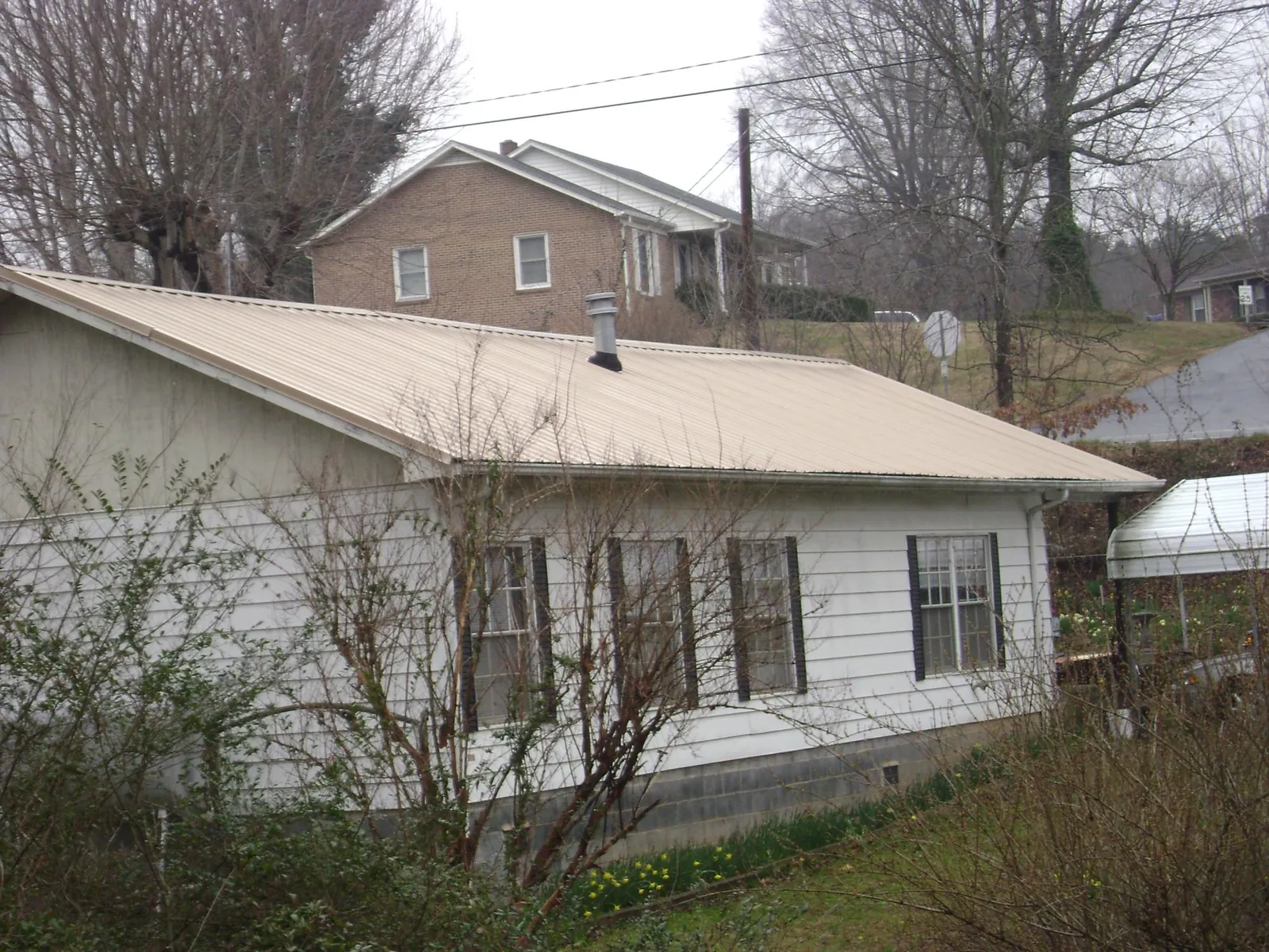 Tan metal roof on a white sided house set into a hillside — Commercial Roofing by Roofing Brothers in Bargersville